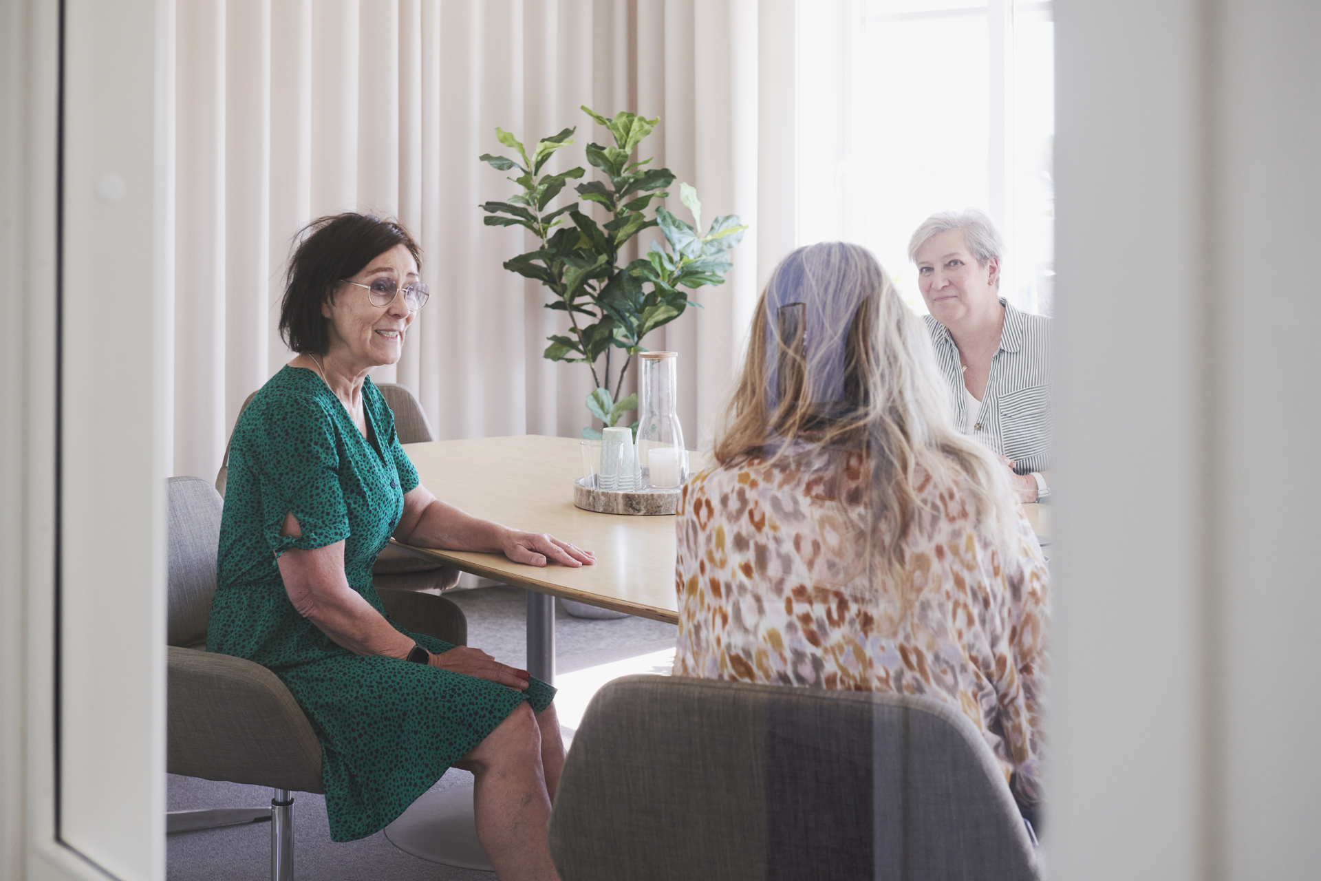 Tre personer sitter runt ett bord i ett mötesrum i kontorsmoduler från Expandia. Rummet är ljust och möblerat med stolar, bord och gröna växter, och samtal pågår i en lugn arbetsmiljö. Bilden är tagen i kontorsmoduler vid Alviks trafik i Luleå.