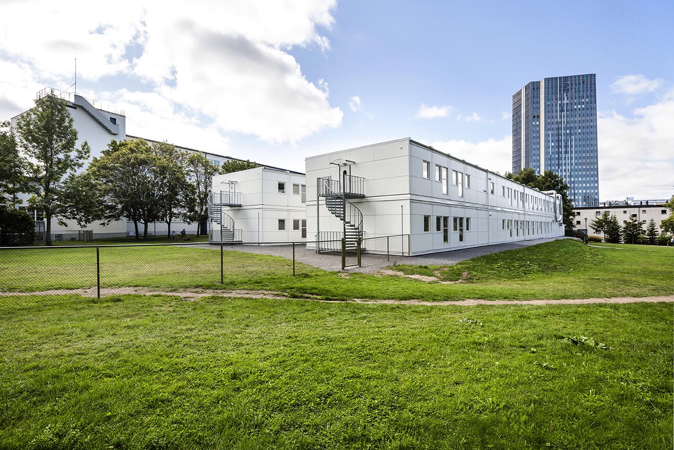 Exteriör vy av Sveaplansskolan i Stockholm, uppförd med skolmoduler från Expandia. Tvåvånings vita modulbyggnader med fönsterrader och externa spiraltrappor i stål står placerade på en grön skolgård. Modulerna visar Expandias flexibla och modulära lösning för utbildningsverksamhet i stadsmiljö.