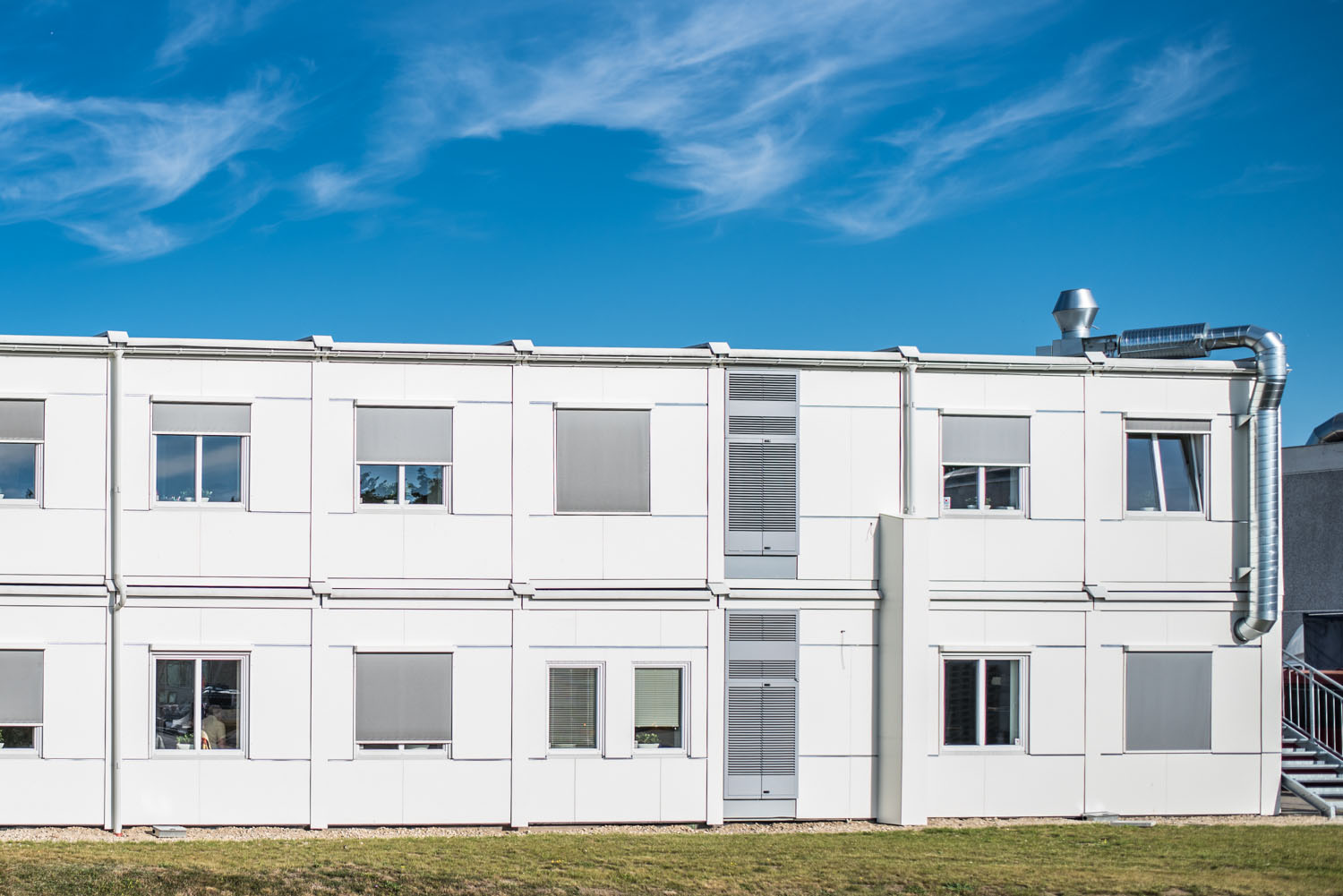 Vita kontorsmoduler i två plan placerade i grön utemiljö. Flexibla kontorsmoduler från Expandia.