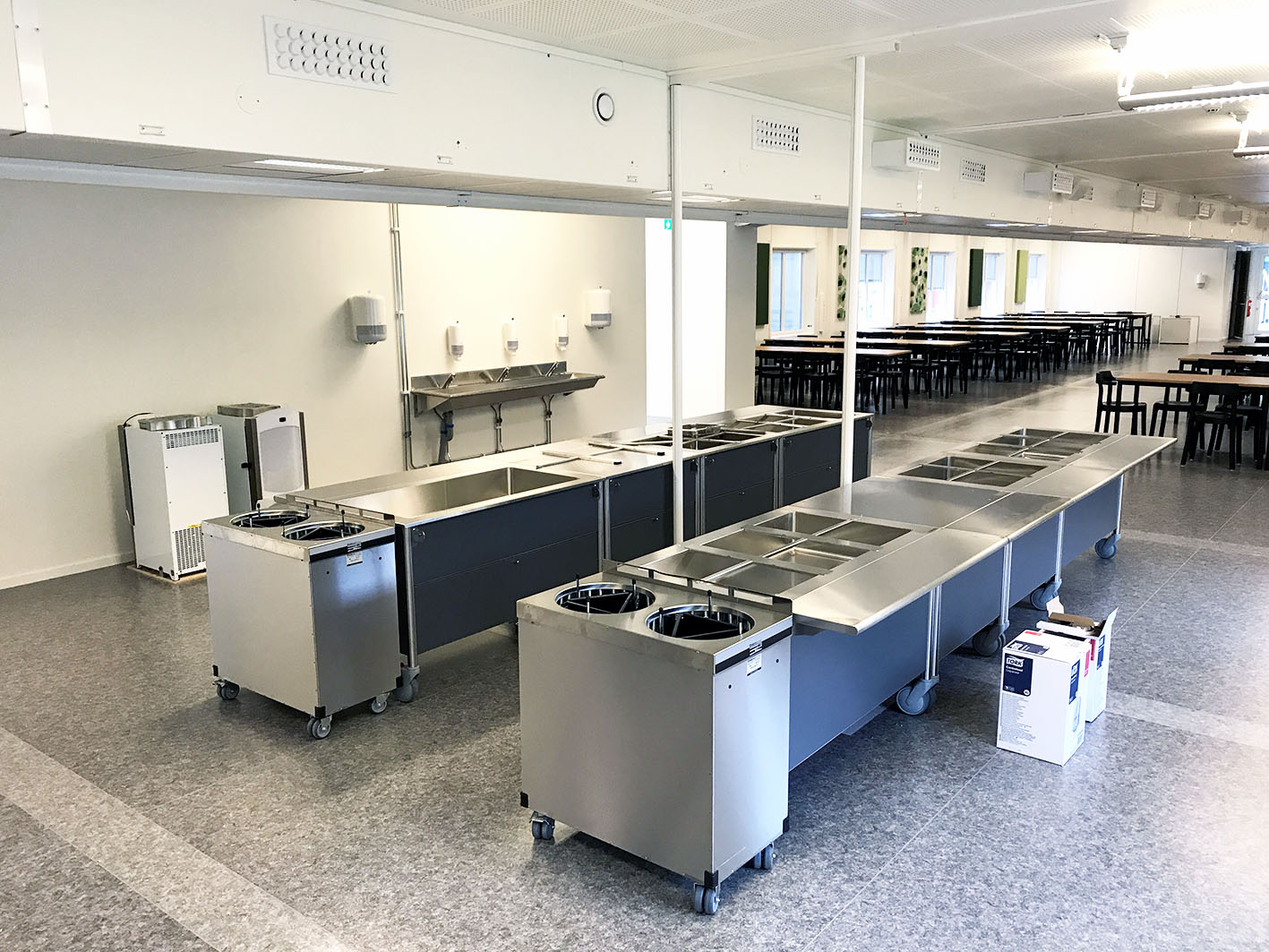 Storkök vid Hultsbergsskolan i Karlstad med serveringslinjer i rostfritt stål och matsal i bakgrunden, inrymt i en flexibel modullösning från Expandia för skolmåltider.