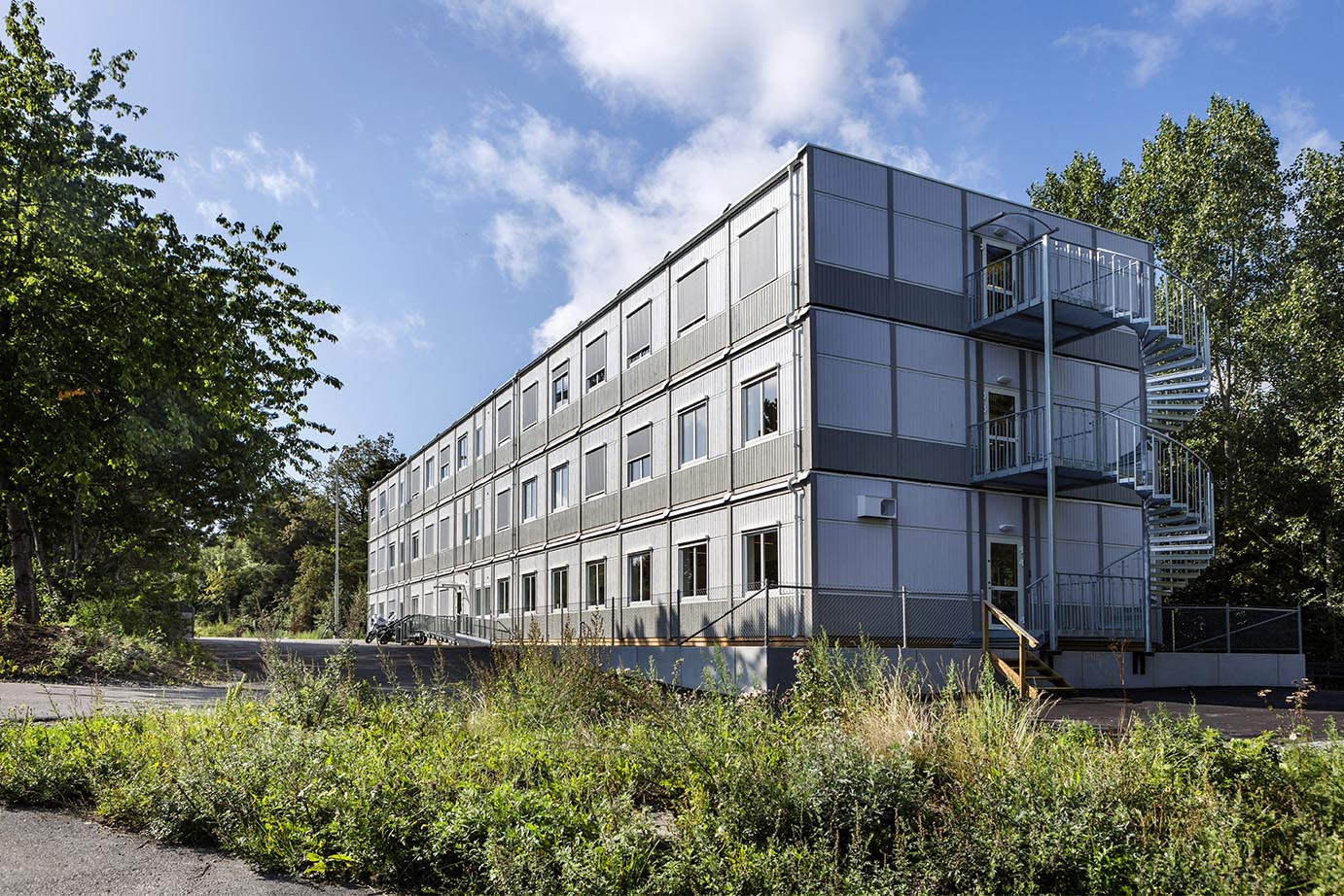 Tillfällig modulbyggnad från Expandia i tre våningar med kontorslokaler, placerad i grön stadsmiljö, med ljus fasad, många fönster och externa trappor.