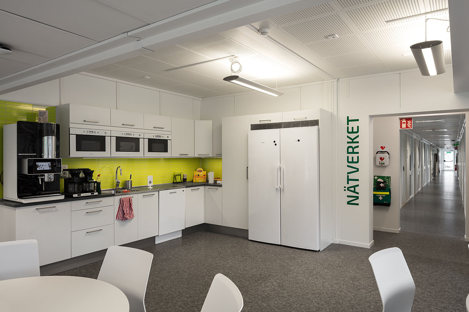 Landskrona Energi Ljust personalrum med köksdel, vita skåp och mikro­vågsugnar, kaffemaskiner, runda bord med vita stolar samt gröna detaljer på väggar och möbler