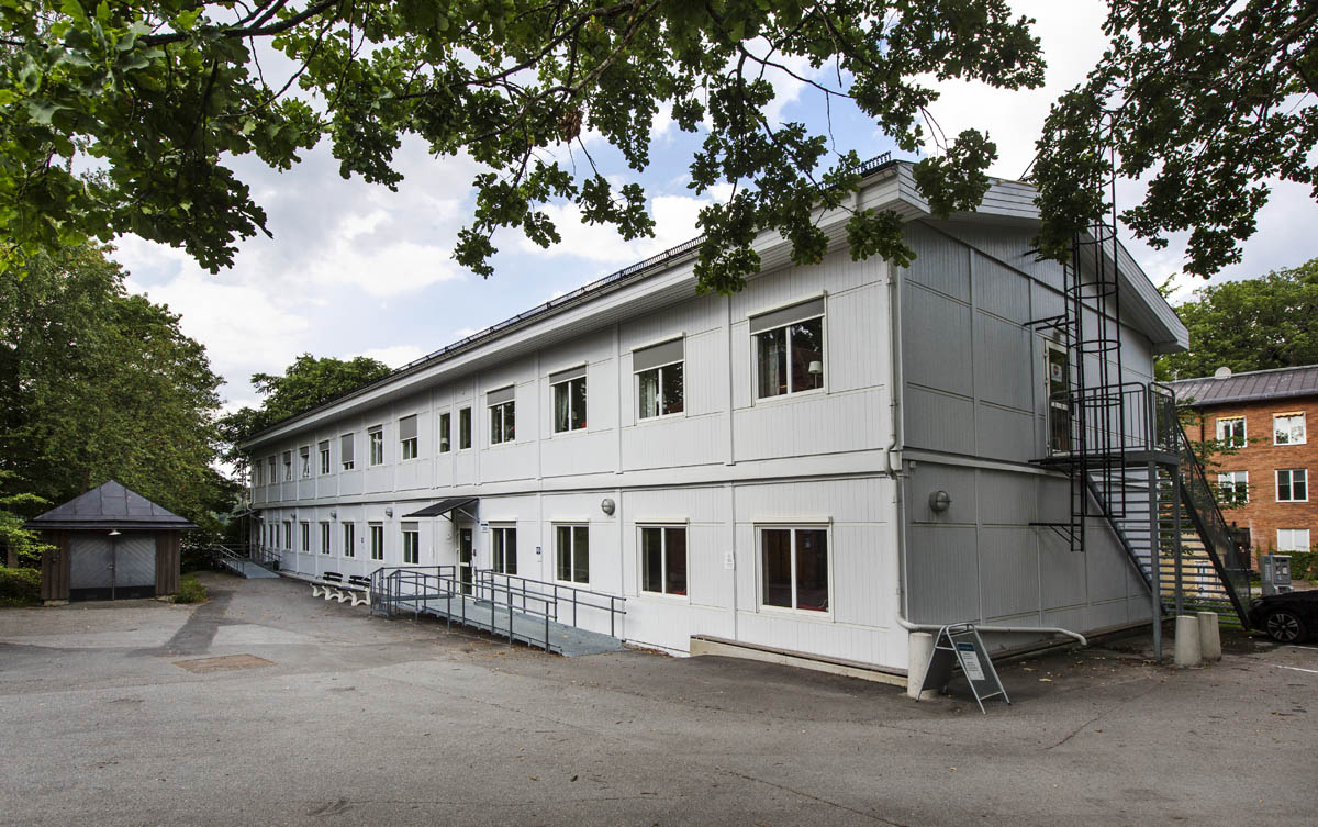 Ljusa kontorsmoduler i två plan med fönsterrader, entré med ramp och räcke, omgivna av grönska och träd i en lugn utemiljö – kontorsmoduler från Expandia.