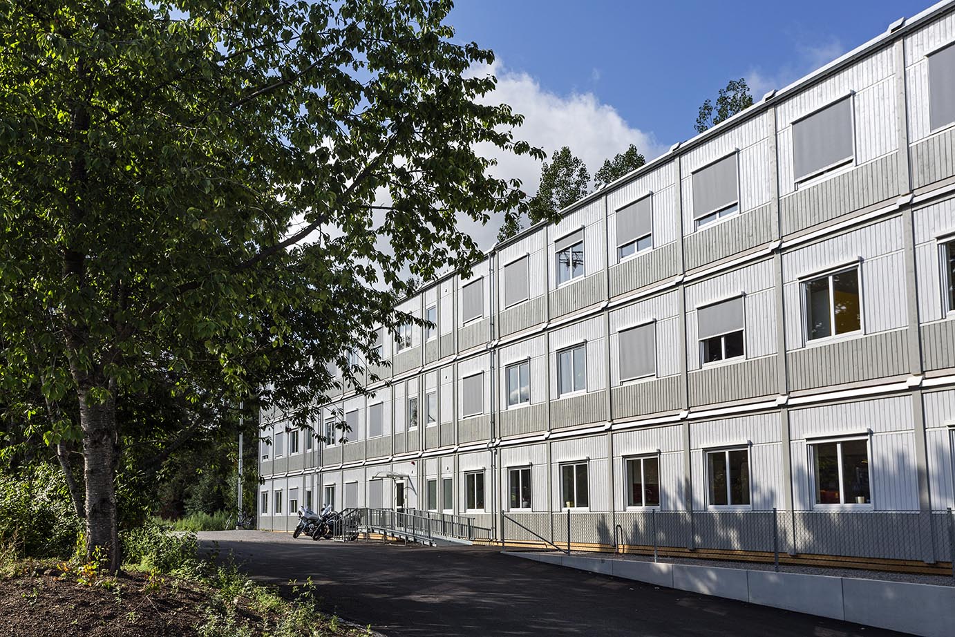 Tillfällig modulbyggnad från Expandia i tre våningar med kontorslokaler, placerad i grön stadsmiljö, med ljus fasad, många fönster och externa trappor.