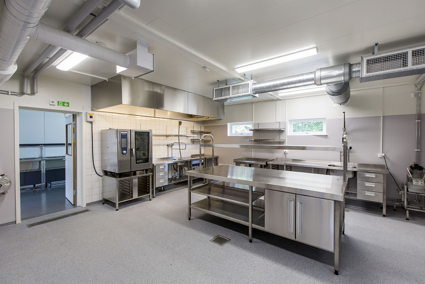 Tillfälligt storkök i Falkbergsskolans modullösning från Expandia, med rostfria arbetsbänkar, ugn, ventilationssystem i taket samt serverings- och diskrum i anslutning.