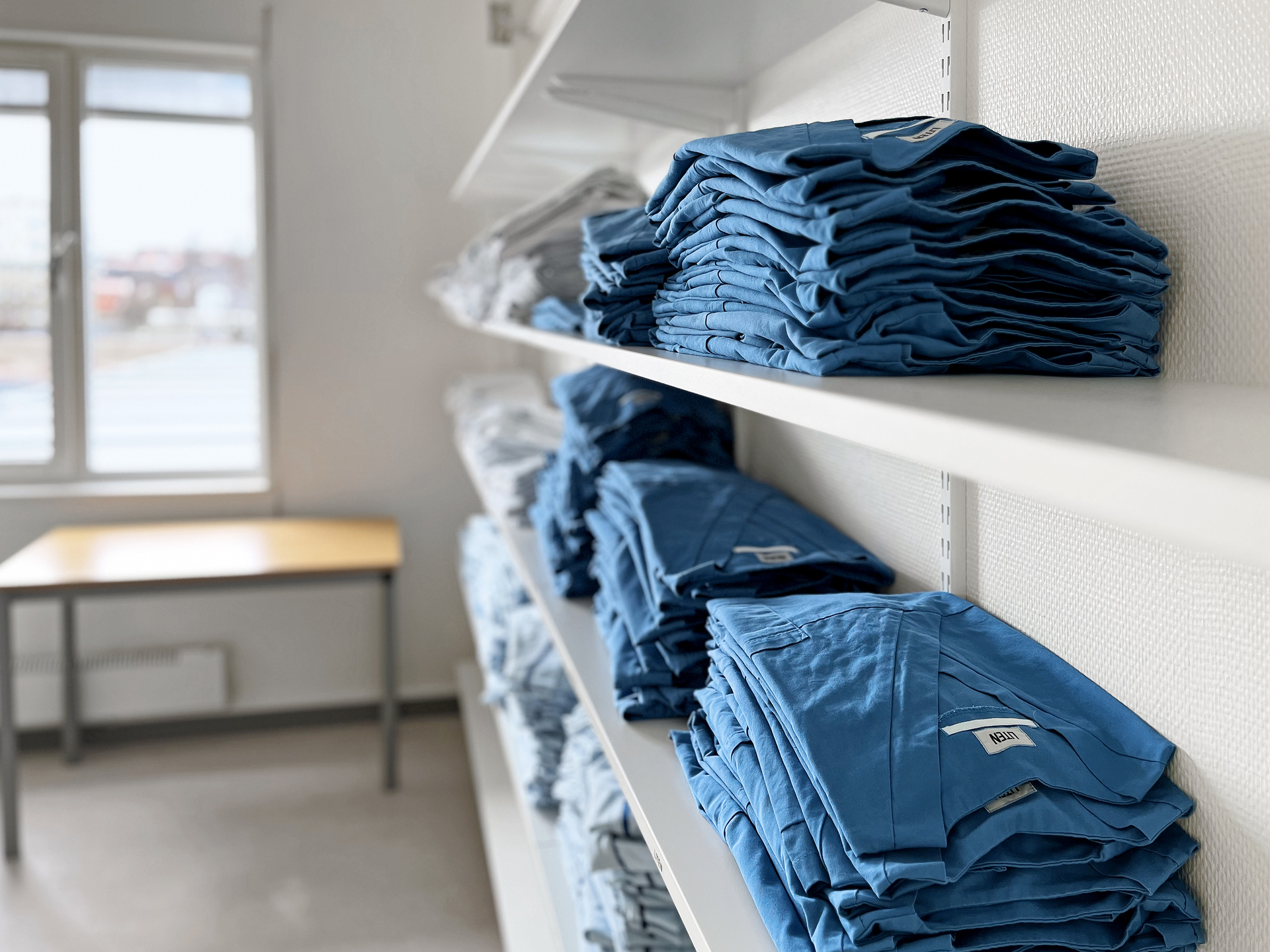 Hylla med vikta arbetskläder i personalutrymme på Skillingaryds vårdcentral, inrymd i moderna och flexibla vårdmoduler från Expandia