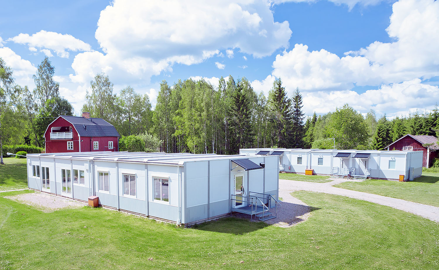 Boendemoduler från Expandia placerade i grön miljö med gräsmattor, gångvägar och omgivande träd, med flera moduler samlade i ett mindre bostadsområde.