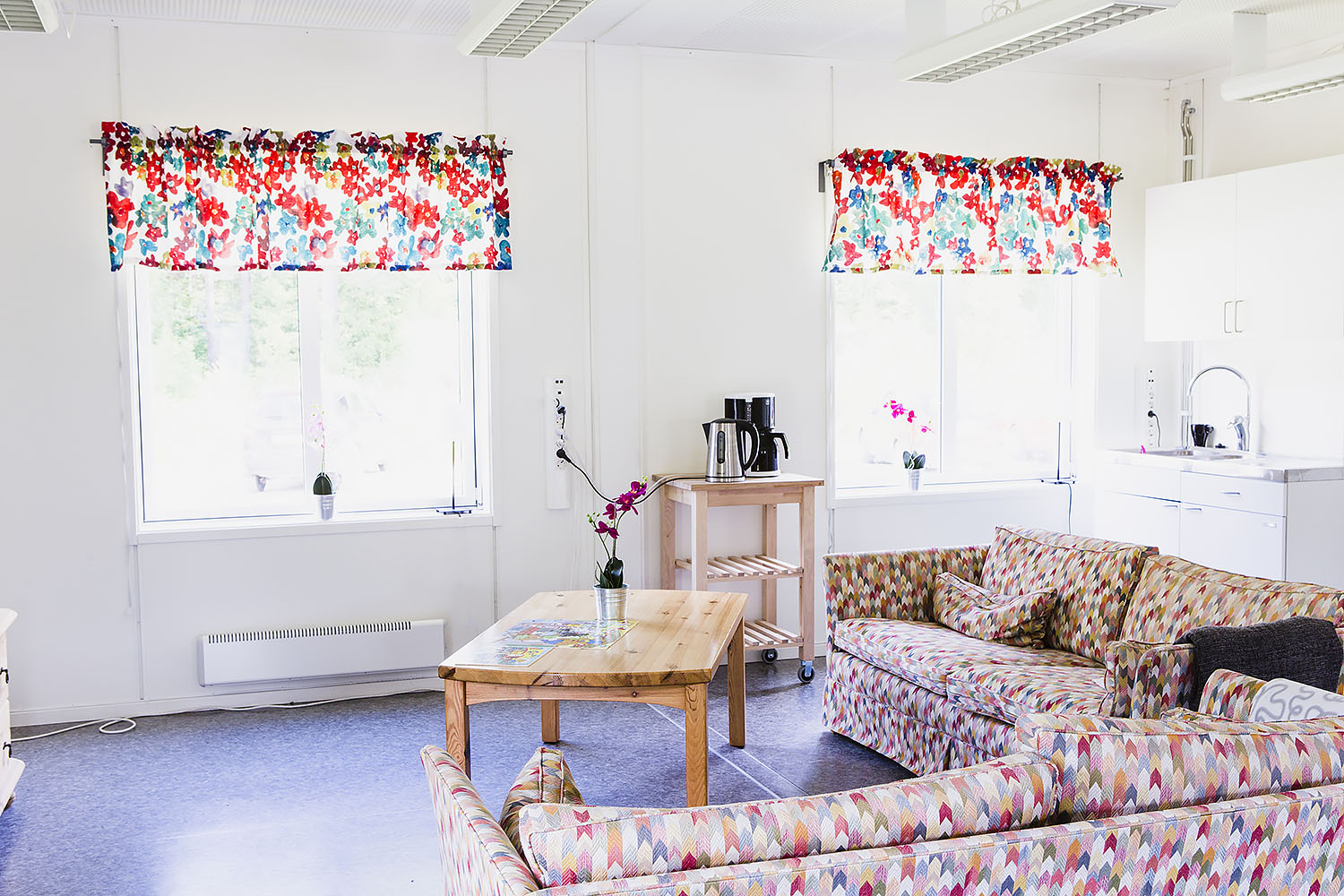 Allrum i boendemoduler från Expandia med soffgrupp, soffbord, kaffestation och fönster med färgglada gardiner.